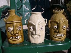 three ceramic masks sitting on top of a green bench next to two vases with faces painted on them