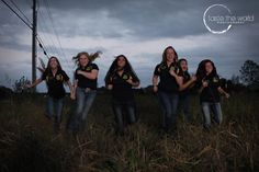 a group of women in black shirts standing on top of a lush green field under a cloudy sky