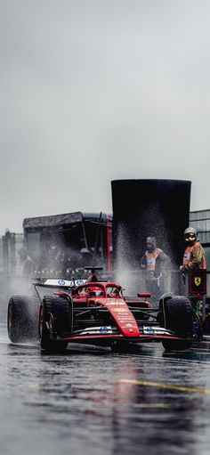 a red race car driving down a wet street next to a truck and some people