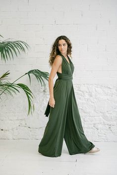 a woman standing in front of a white brick wall wearing a green jumpsuit and sneakers