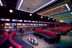 a bowling alley with red couches and televisions on the wall behind them,