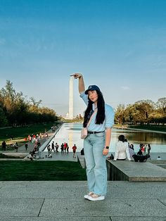 a woman standing in front of the washington monument with her hand up to the sky