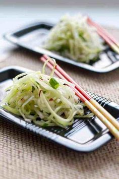 two black trays filled with food and chopsticks on top of a table