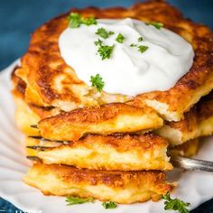 a stack of pancakes with sour cream and parsley on top, sitting on a white plate