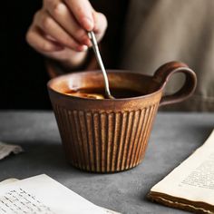 a person is spooning something into a bowl on a table with an open book