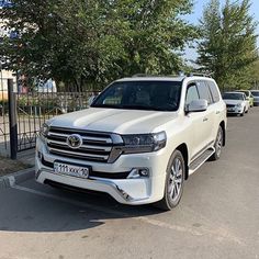 a white toyota land cruiser parked in front of a fenced off parking lot with cars behind it