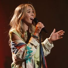 a woman singing into a microphone while holding her hands out in front of her face