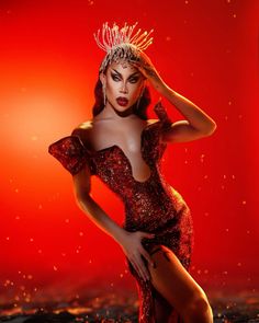 a woman in a red dress with a crown on her head and hands behind her head