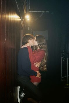 two people are kissing in the dark, one is wearing a red dress and the other has a blue shirt