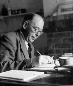 a man sitting at a table writing in a book with a cup on top of it