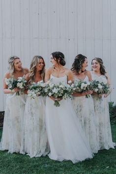 a group of women standing next to each other in front of a white wall holding bouquets