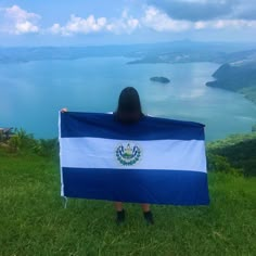 a woman holding a flag in front of her face while standing on top of a hill