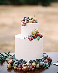 a three tiered wedding cake with grapes and berries on the top is surrounded by greenery