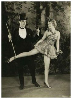 an old photo of a man and woman dressed in fancy clothing posing for the camera