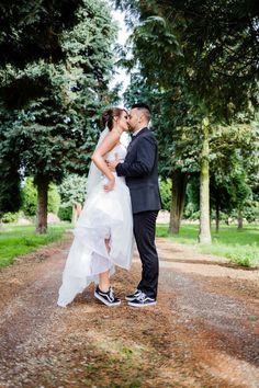 a bride and groom kissing in the middle of a dirt road with trees behind them