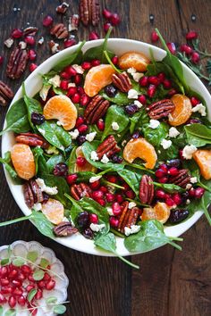 a salad with oranges, spinach and pecans in a white bowl on a wooden table