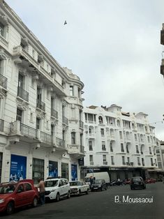 several cars parked on the side of a street in front of tall white buildings with balconies