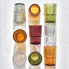 several different colored glass cups and saucers lined up in a row on a white surface