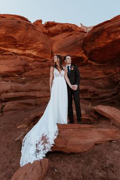 a bride and groom standing in front of red rocks