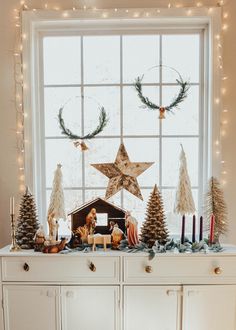 a white dresser topped with christmas decorations and candles next to a window covered in lights