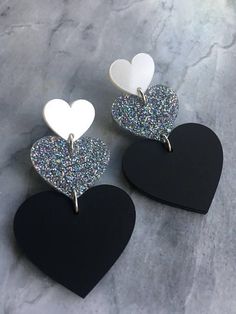 three black and white heart shaped earrings on a marble surface with glitter in the middle