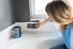 a woman in blue shirt painting a white sink with black and gray paint on it