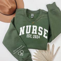 a green sweatshirt with the word nurse on it next to a hat and palm leaf