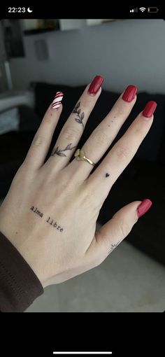 a woman's hand with red fingernails and tattoos on her left thumb, showing the ring finger tattoo