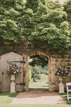 an outdoor ceremony with flowers and greenery on the wall, in front of a stone archway