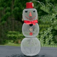 a snowman made out of wire sitting on top of a table next to trees