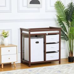 a baby crib with white storage bins next to a potted plant