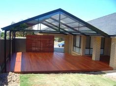 a wooden deck in front of a house with a metal roof and glass walls on it