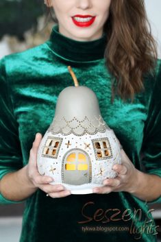 a woman is holding a doll house in her hands and wearing a green velvet dress