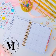 an open planner next to some pens and pencils on a white table with pink streamers