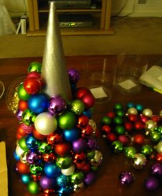 a christmas tree made out of ornaments on a table next to a wine glass and silver cone