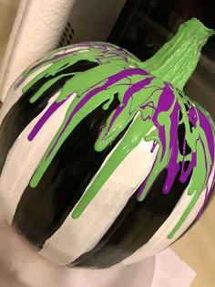 a painted pumpkin sitting on top of a white table next to a vase filled with green and purple liquid