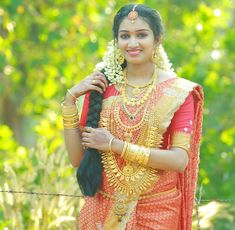 a woman in an orange and red sari holding a black bag with gold jewelry on it