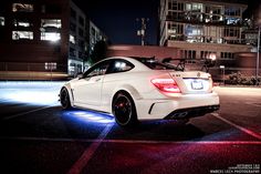 a white mercedes cla parked in a parking lot at night with its lights on