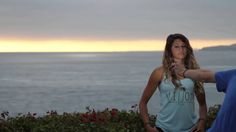 a man and woman standing next to each other in front of the ocean at sunset