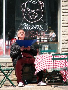 a man sitting in front of a restaurant reading a menu while holding a clipboard