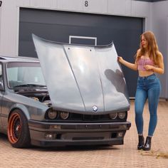 a woman standing next to a car with its hood open