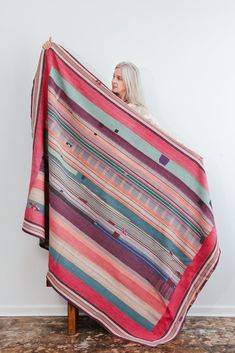 a woman holding up a multicolored striped blanket