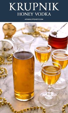 three glasses filled with honey vodka on top of a marble table next to gold beads