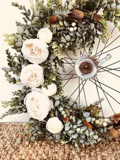 a bicycle wheel decorated with white flowers and pine cones on top of a straw mat