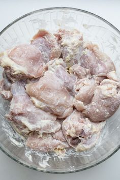 raw chicken pieces in a glass bowl on a white table top, ready to be cooked