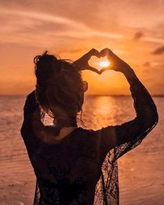 a woman making a heart shape with her hands on the beach at sunset or sunrise