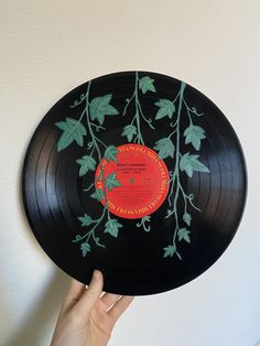 a person holding up a black record with green leaves and red disc label on it