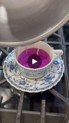 a purple tea cup sitting on top of a blue and white saucer next to a stove