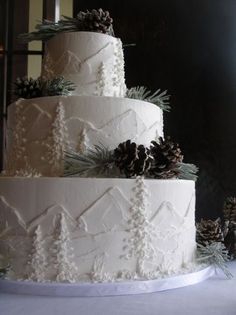 a three tiered white wedding cake with pine cones on top