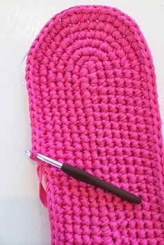 a pink crochet bag with a black handle and a pen resting on it